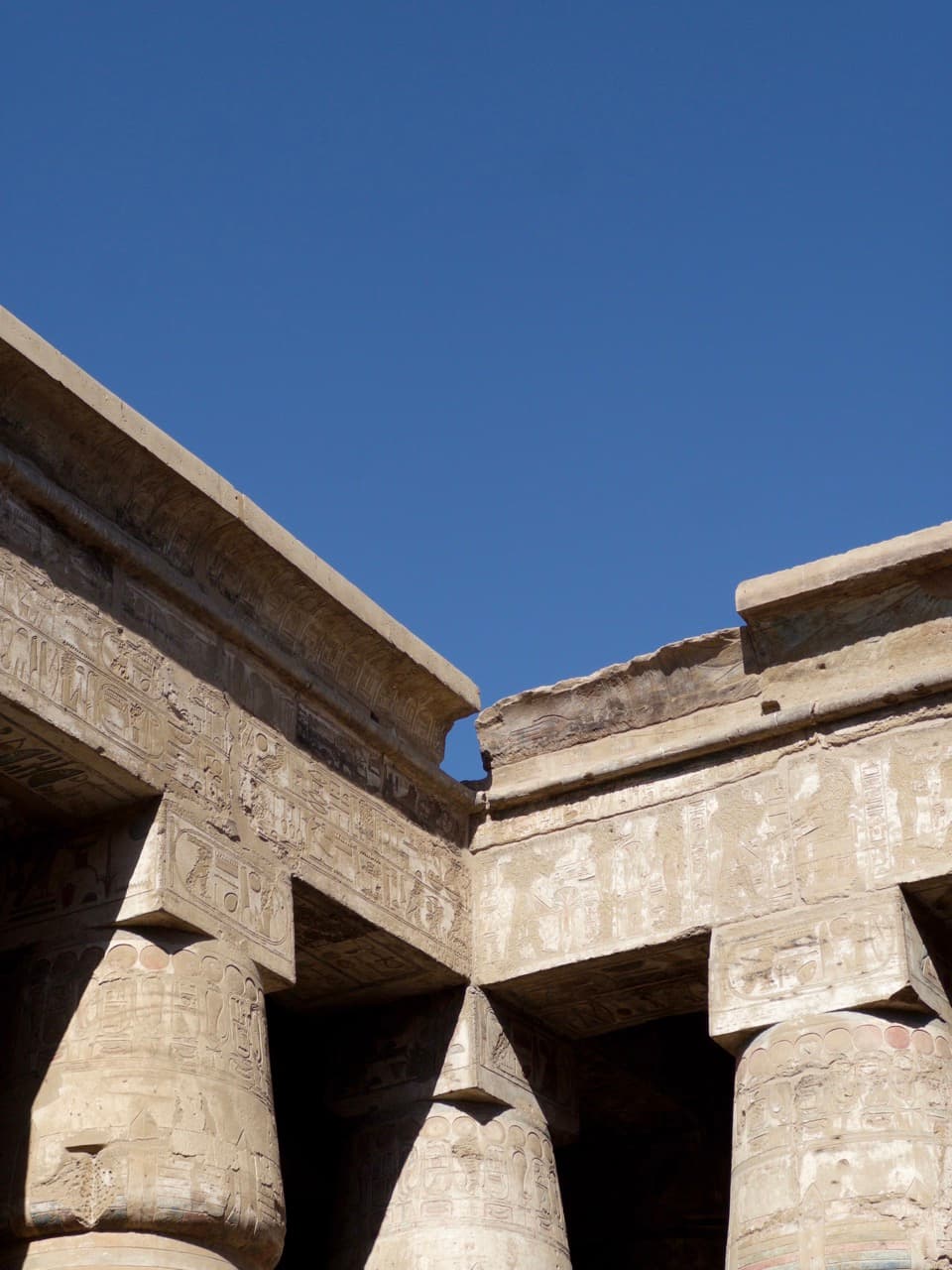 Massive stone columns and lintels of an ancient Egyptian temple carved with hieroglyphs against a deep blue sky